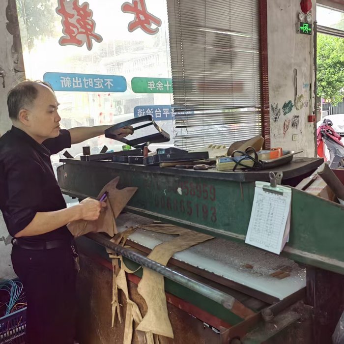 Workers cutting upper components from leather panels at a cutting table in a footwear workshop